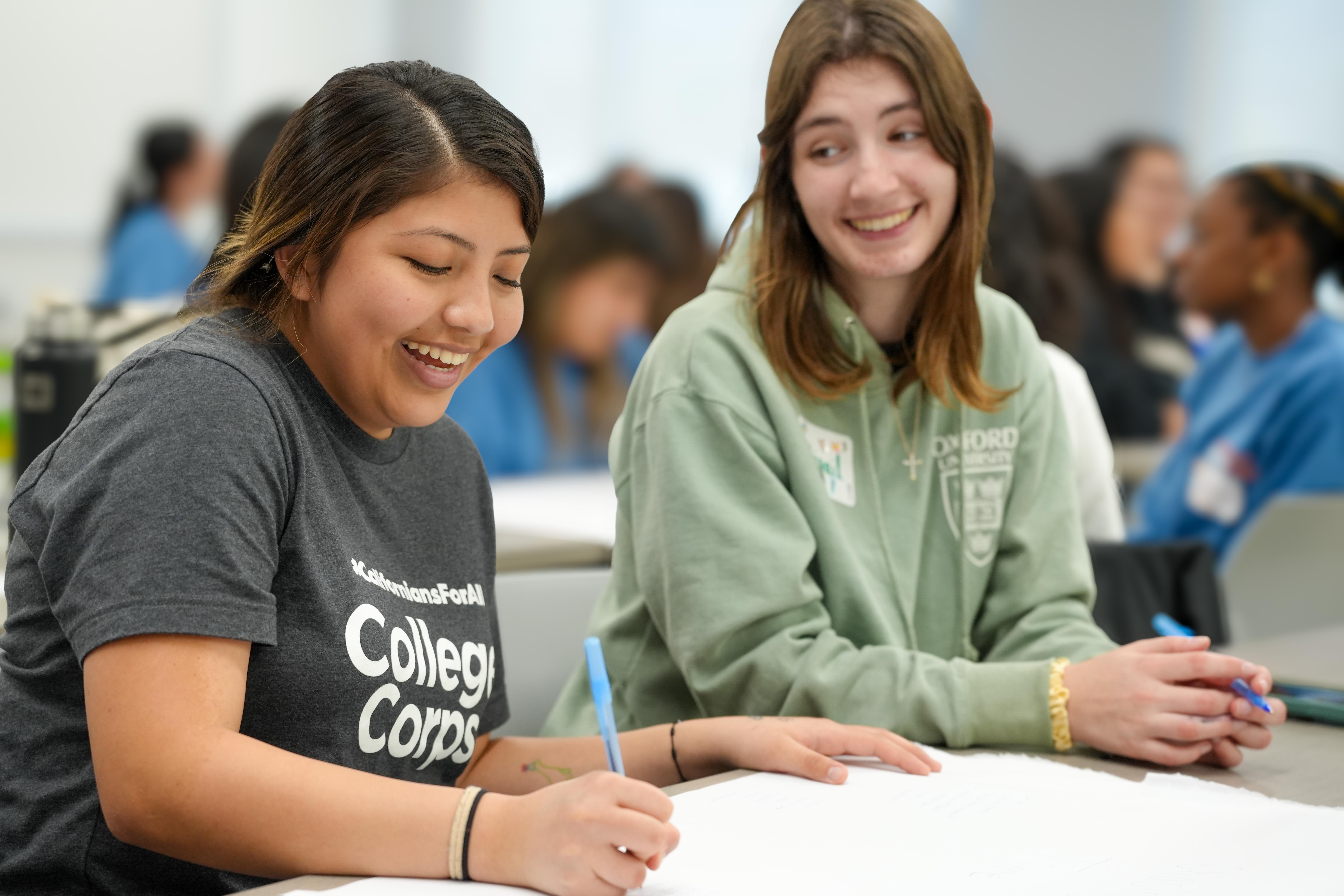 Two College Corps fellows smiling sitting at a table